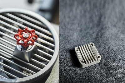 Metallic valve handle with red accents on a metallic surface, next to a smaller metallic component on a textured fabric background.